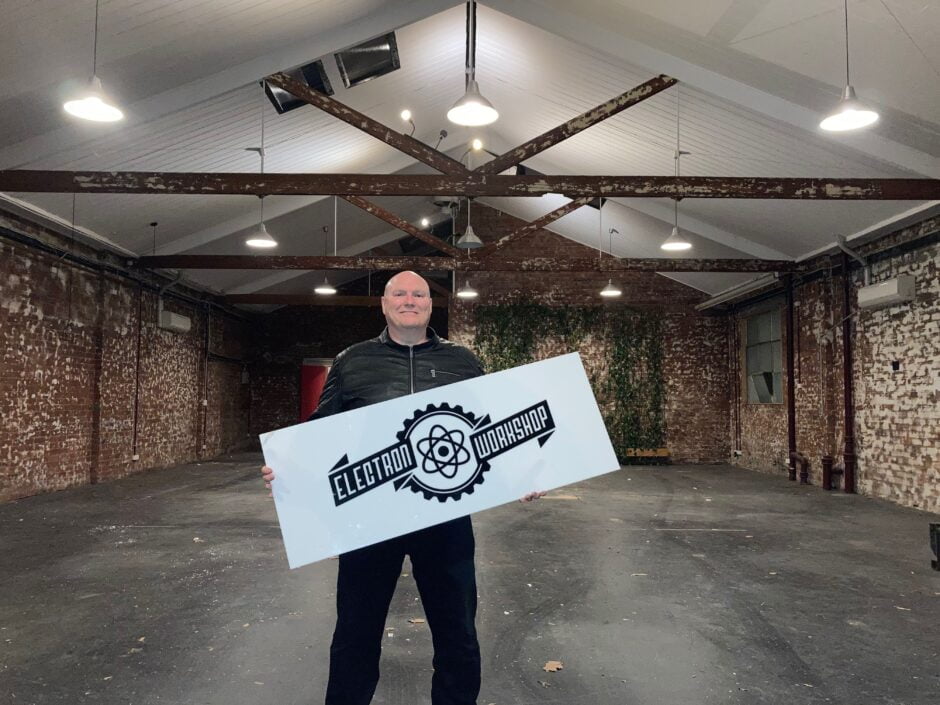 Marty standing in an empty Electron Workshop with the Electron Workshop sign from our lightbox that was mounted in the green wall.